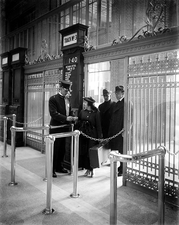 3 passengers in formal winter coats and hats pass through a gate and have their tickets taken by a railway employee